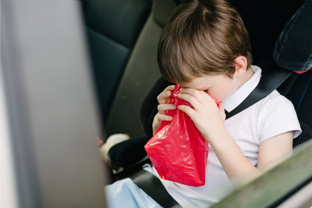 Criança no carro vomitando em uma sacola. 