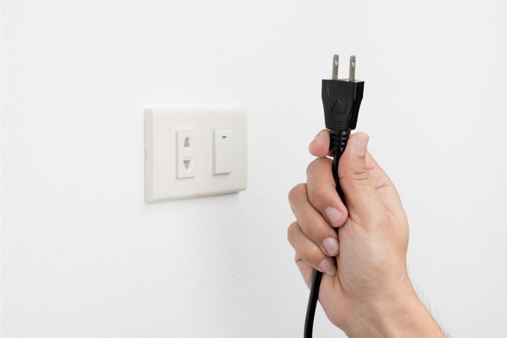 Pessoa segurando um plug ao lado de uma tomada.