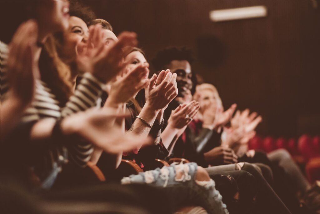 Pessoas da plateia de um teatro aplaudindo.