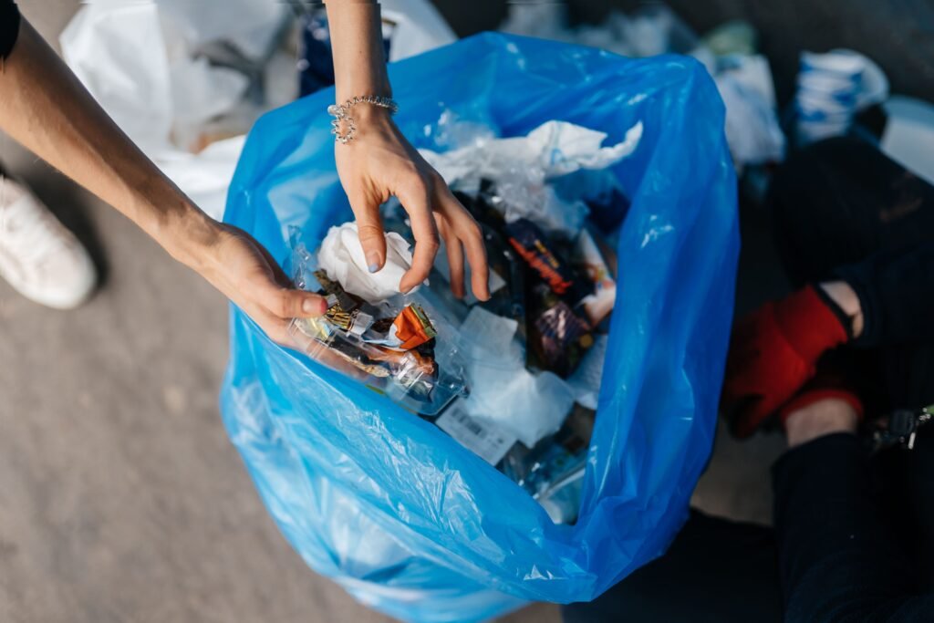 Pessoa jogando lixo em um saco azul.
