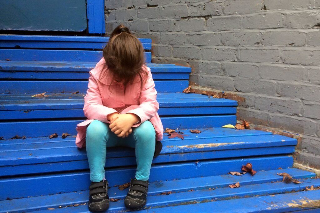 Criança sentada triste em um degrau.