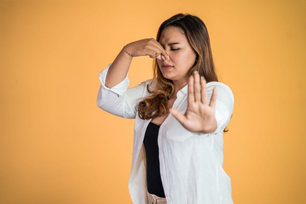 Mulher em um fundo laranja fechando o nariz.