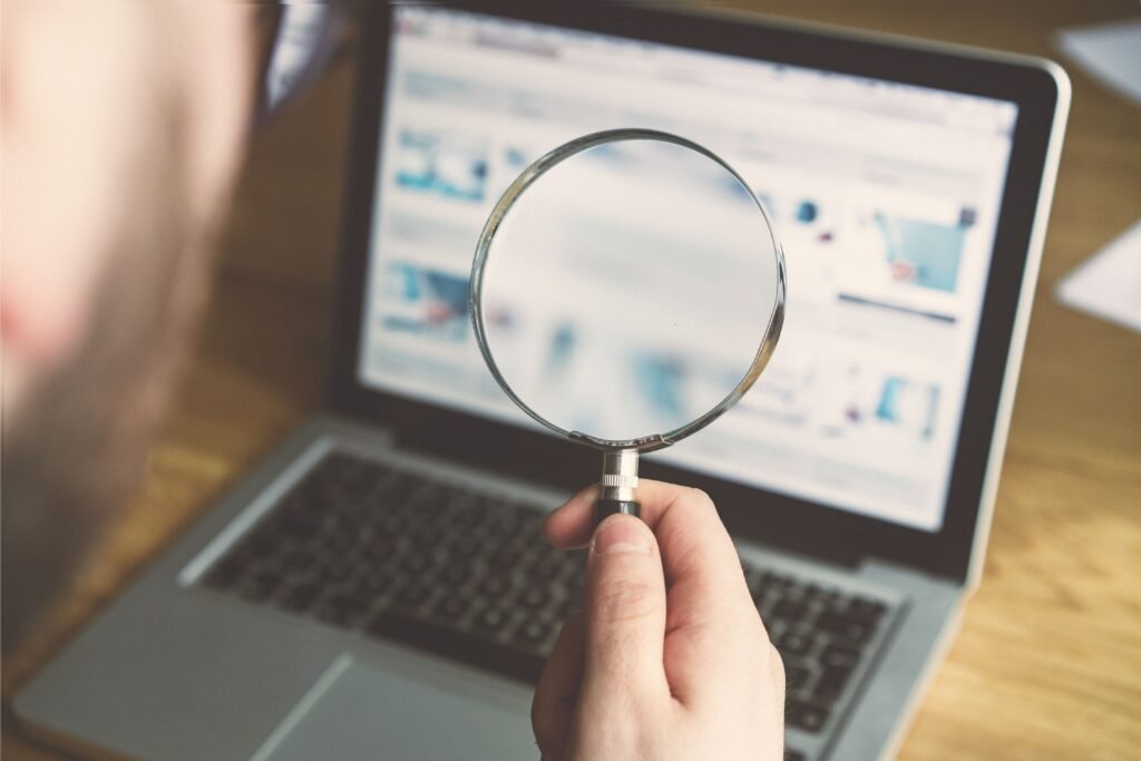 Pessoa com uma lupa olhando um notebook.